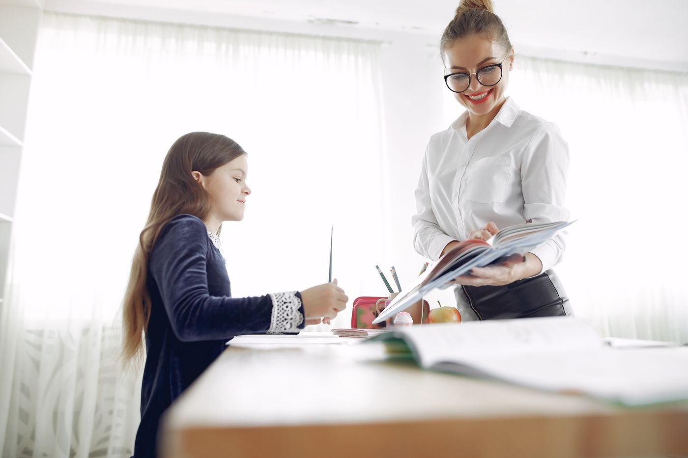 Educatoare care explică tema unei fete la birou, în sala de studiu